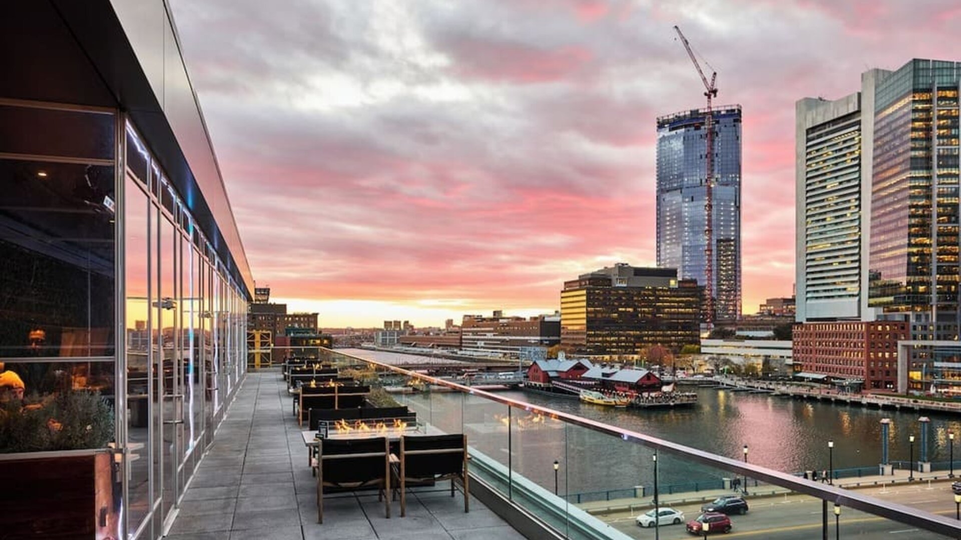 Panoramic rooftop terrace view featuring Boston skyline and waterfront scenery at sunset from The Envoy Hotel, Autograph Collection.