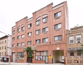 Wide exterior shot of Phoenix Hotel Brooklyn Sunset Park showcasing the multi-story brick building with on-site parking access.