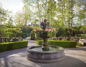 Beautiful landscaped garden courtyard with a decorative fountain surrounded by lush greenery and outdoor seating at The Garland.