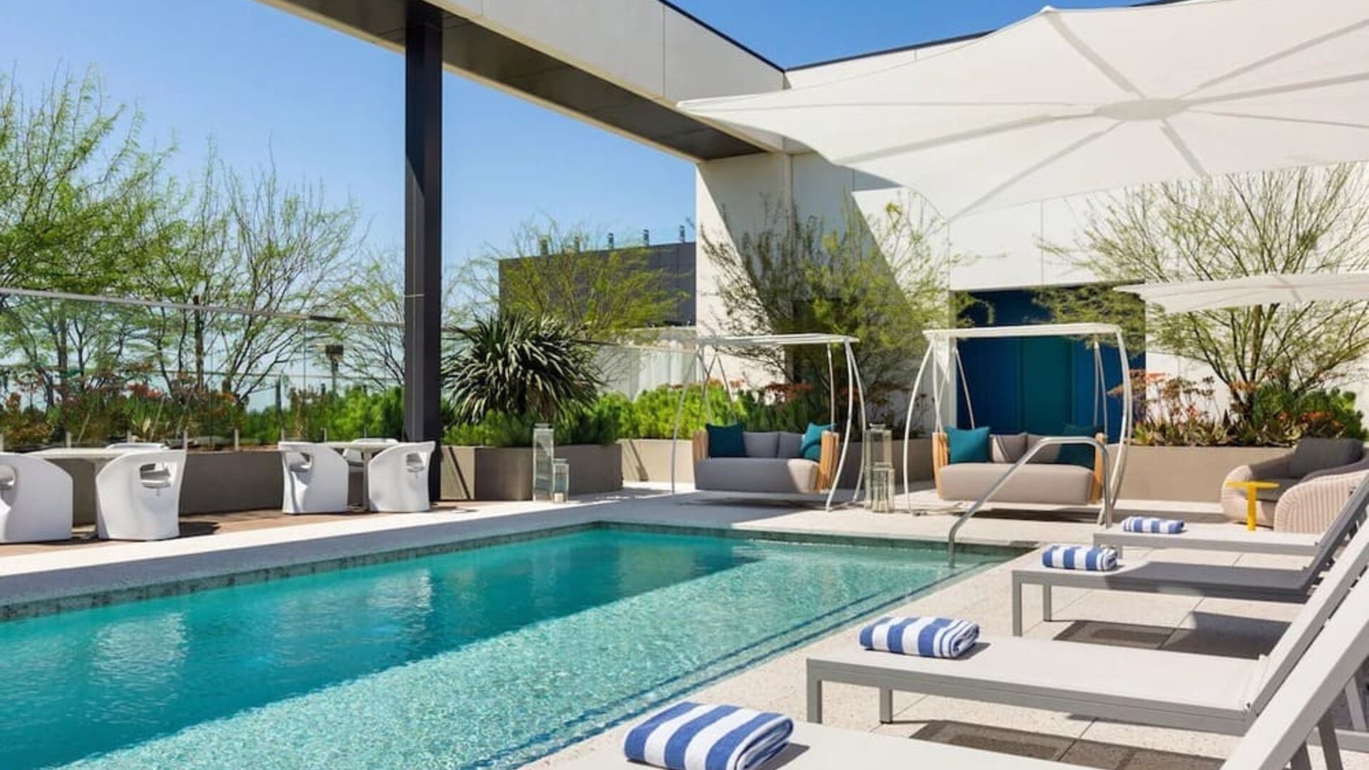 Outdoor rooftop-style swimming pool surrounded by sun loungers, shaded cabanas, and landscaped relaxation areas.