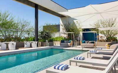 Outdoor rooftop-style swimming pool surrounded by sun loungers, shaded cabanas, and landscaped relaxation areas.