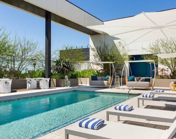 Outdoor rooftop-style swimming pool surrounded by sun loungers, shaded cabanas, and landscaped relaxation areas.