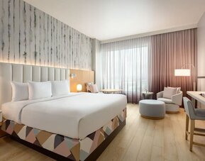 Guest room with a king-size bed, seating area, work desk, and floor-to-ceiling windows offering a bright and relaxing environment.