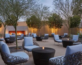Outdoor courtyard lounge area offering comfortable woven seating, cocktail tables, landscaped surroundings, and a fireplace creating a relaxing social atmosphere.
