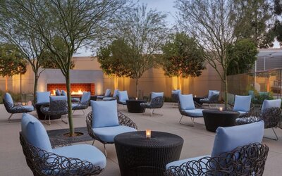 Outdoor courtyard lounge area offering comfortable woven seating, cocktail tables, landscaped surroundings, and a fireplace creating a relaxing social atmosphere.
