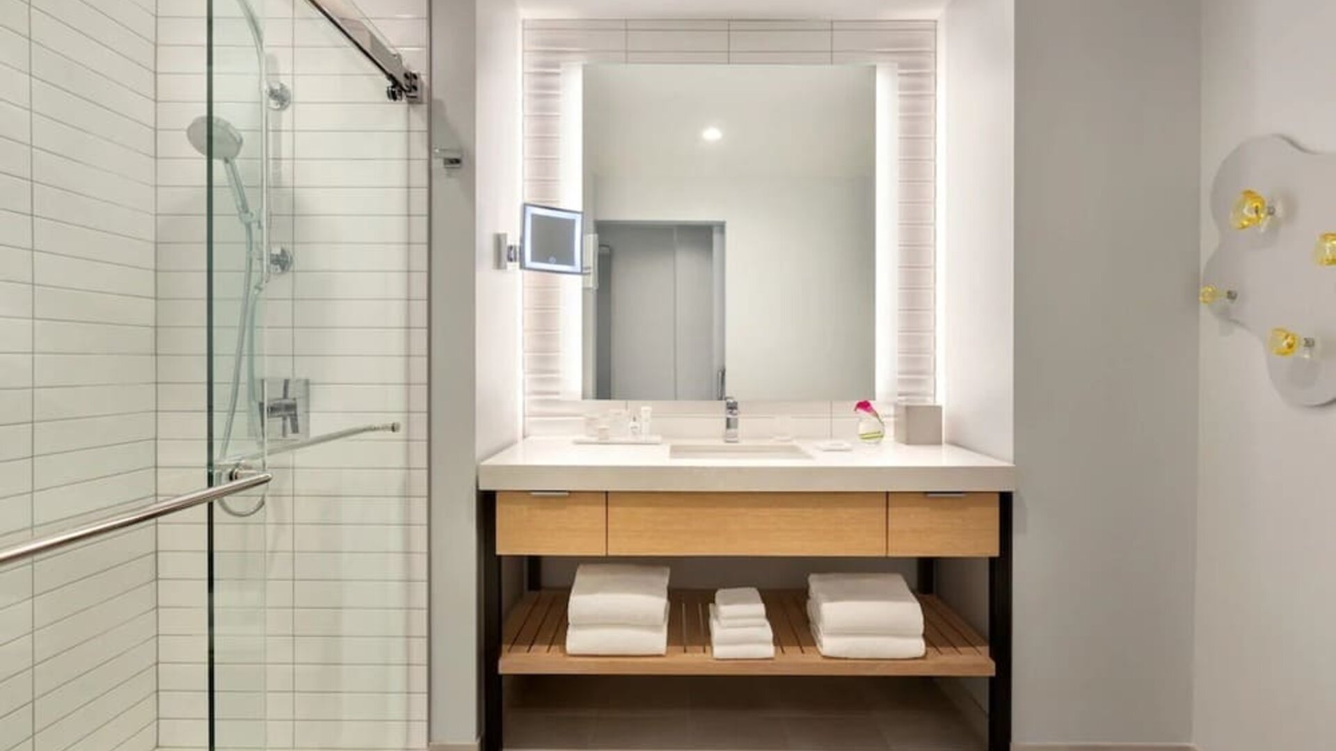 Modern bathroom at The Viv Hotel, Anaheim, A Tribute Portfolio Hotel featuring a spacious vanity, illuminated mirror, walk-in glass shower, and contemporary finishes.