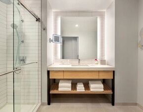 Modern bathroom at The Viv Hotel, Anaheim, A Tribute Portfolio Hotel featuring a spacious vanity, illuminated mirror, walk-in glass shower, and contemporary finishes.