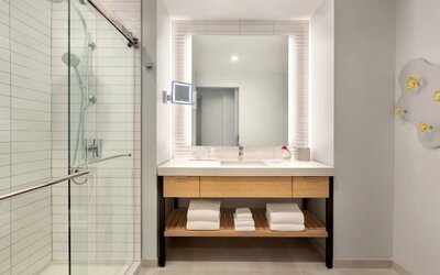 Modern bathroom at The Viv Hotel, Anaheim, A Tribute Portfolio Hotel featuring a spacious vanity, illuminated mirror, walk-in glass shower, and contemporary finishes.