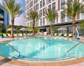 Resort-style pool area surrounded by palm trees, lounge chairs, and private seating areas, creating a relaxing outdoor retreat.