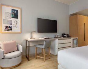 In-room workspace and entertainment area featuring a large flat-screen television, desk, seating, and convenient storage amenities.