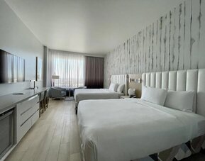 Alternative view of a double-queen guest room highlighting the modern décor, premium bedding, and spacious layout.