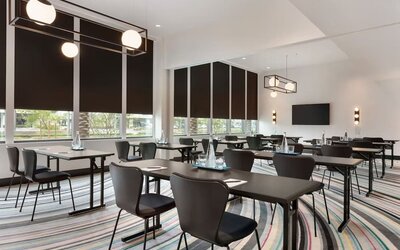 Contemporary meeting room at The Viv Hotel, Anaheim, A Tribute Portfolio Hotel featuring flexible conference-style seating, natural light, modern lighting fixtures, and presentation facilities for business meetings and events.