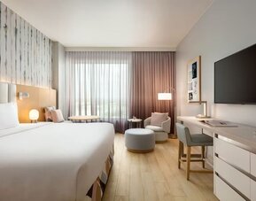Bright king guest room with floor-to-ceiling windows, a dedicated workspace, comfortable lounge seating, and contemporary décor accented by soft pastel tones.