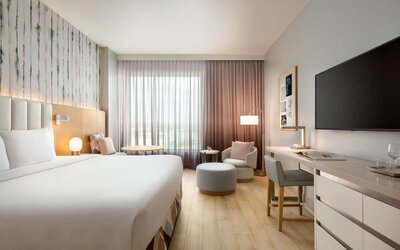 Bright king guest room with floor-to-ceiling windows, a dedicated workspace, comfortable lounge seating, and contemporary décor accented by soft pastel tones.