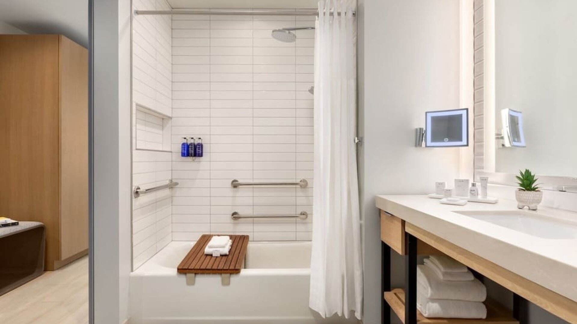 Modern guest bathroom featuring a spacious vanity, illuminated mirror, bathtub and shower combination, and contemporary accessibility-friendly design elements.