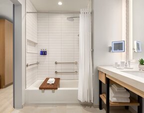 Modern guest bathroom featuring a spacious vanity, illuminated mirror, bathtub and shower combination, and contemporary accessibility-friendly design elements.
