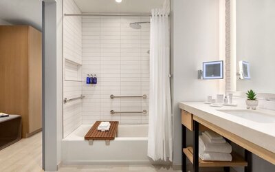Modern guest bathroom featuring a spacious vanity, illuminated mirror, bathtub and shower combination, and contemporary accessibility-friendly design elements.