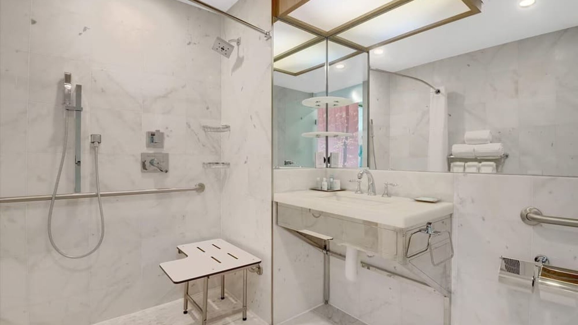 Accessible guest bathroom at Wyndham Garden Brooklyn Sunset Park featuring a roll-in shower, safety grab bars, shower seating, marble finishes, and a spacious vanity designed for comfort and accessibility.