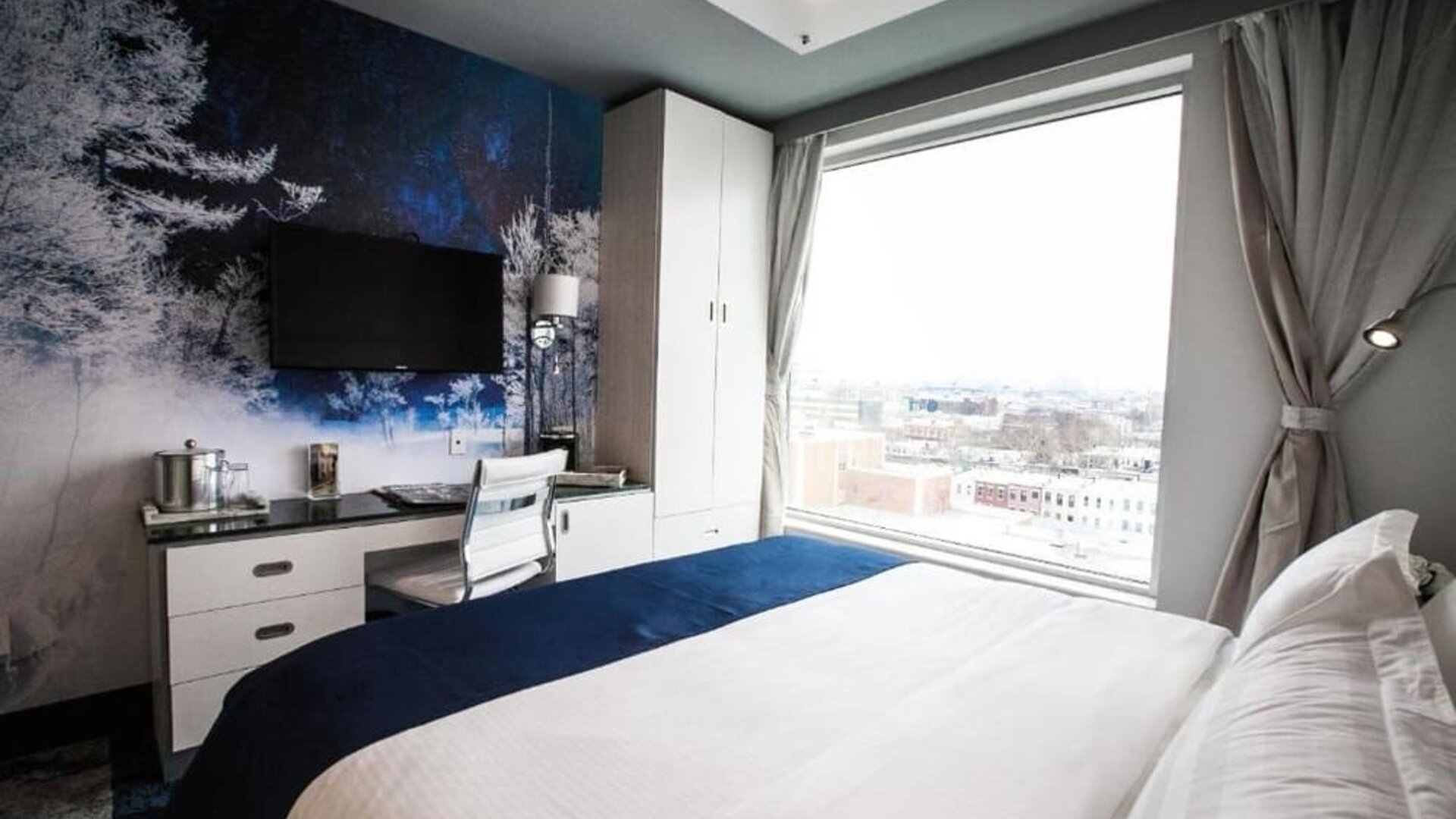 Contemporary king guest room with floor-to-ceiling windows, city views, a dedicated workspace, wall-mounted television, and modern nature-inspired décor.
