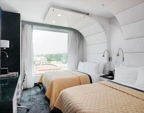 Double-queen guest room featuring two beds, large windows, reading lights, modern furnishings, and a comfortable layout suitable for families or groups.