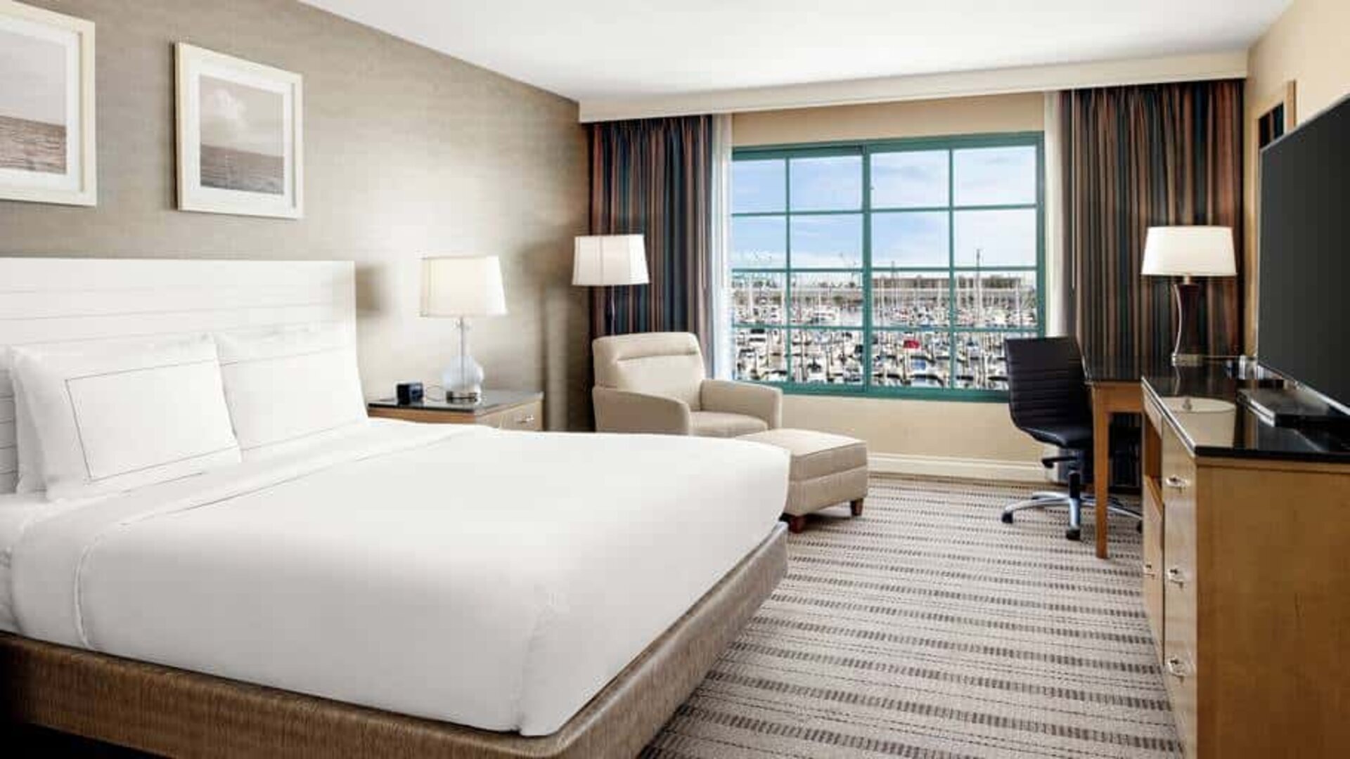 Bright queen suite hotel room with workspace and prime view of San Pedro port and marina.