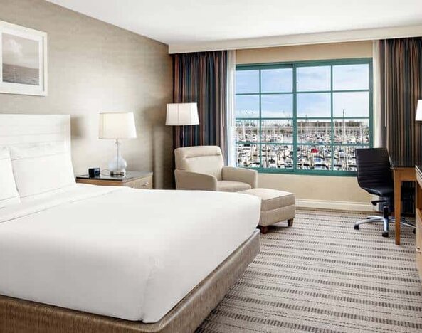 Bright queen suite hotel room with workspace and prime view of San Pedro port and marina.