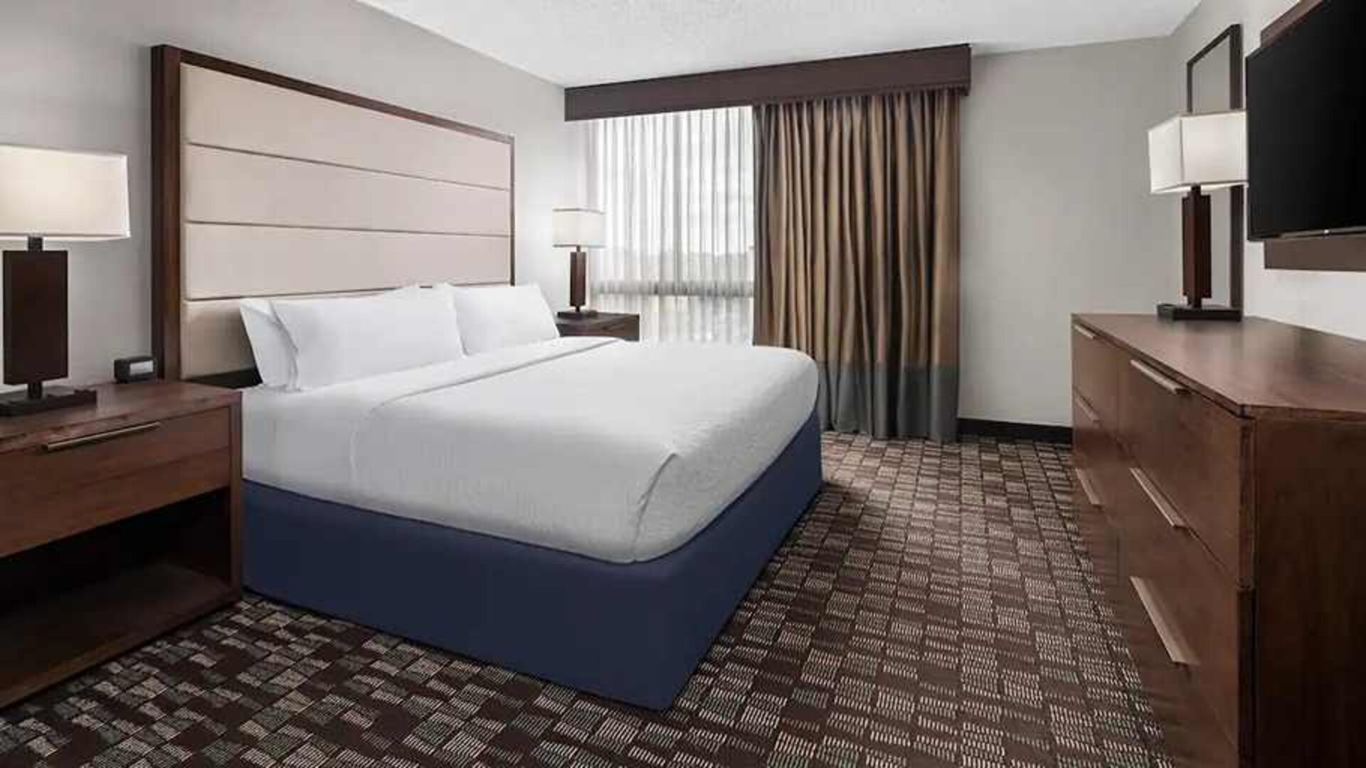 King-sized room with natural light, TV, and work desk at Embassy Suites by Hilton Nashville Airport.