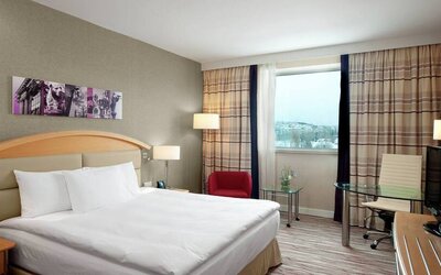 Tan walls, king-size bed with desk area to work and corner window view.