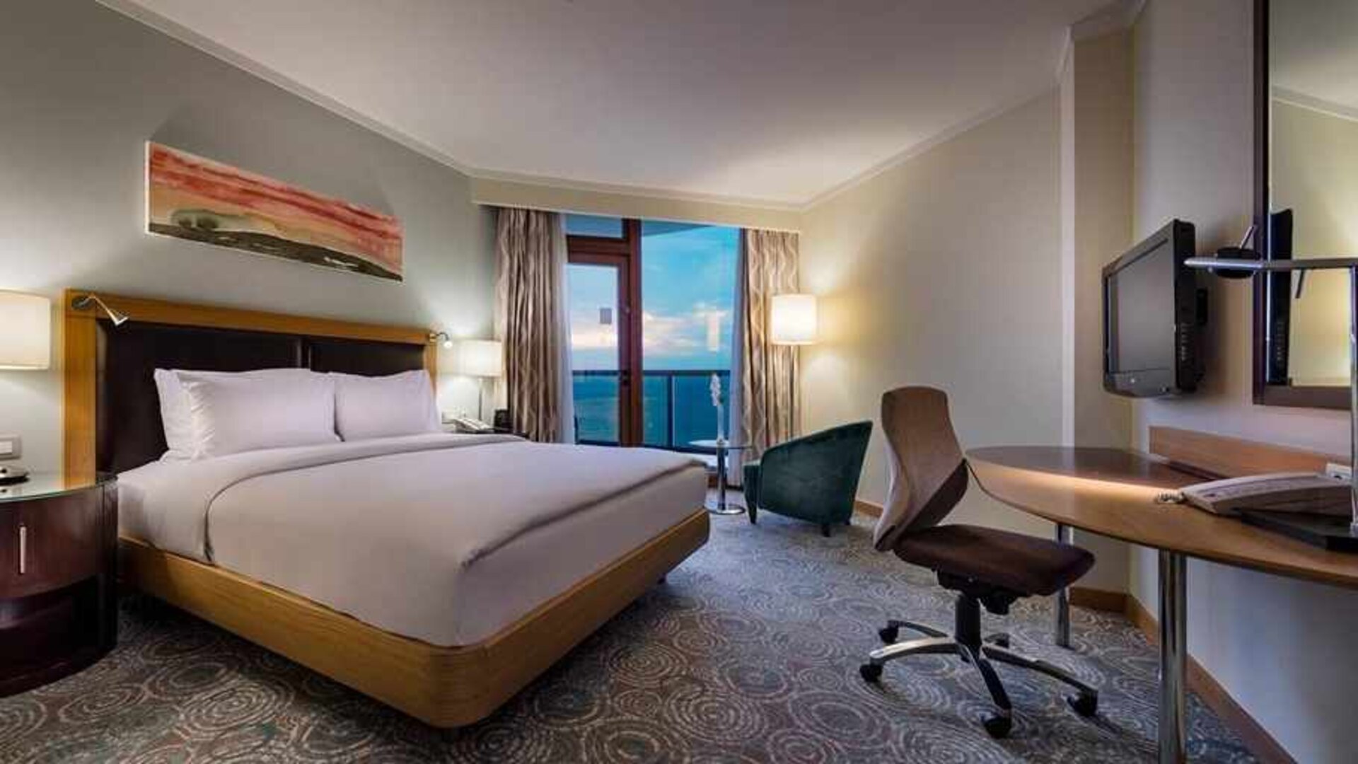 spacious king room with TV, desk, chair, and lots of natural light at Mersin HiltonSA.