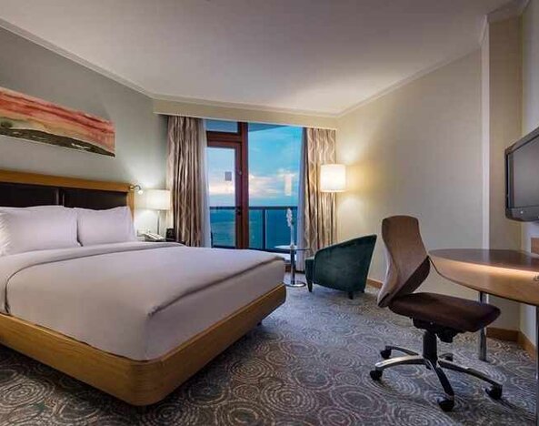 spacious king room with TV, desk, chair, and lots of natural light at Mersin HiltonSA.