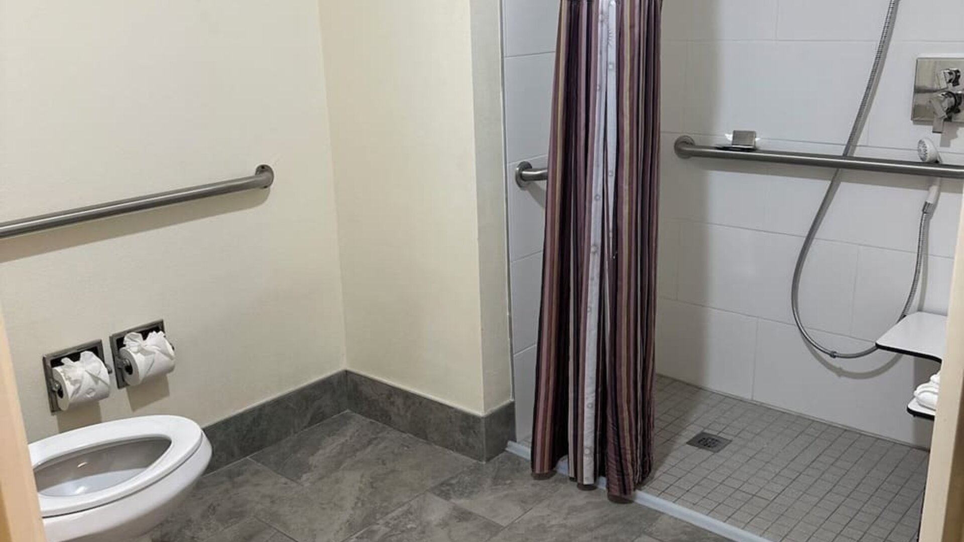 Accessible bathroom featuring a roll-in shower, safety grab bars, and spacious layout designed to provide comfort and convenience for all guests at La Quinta Inn & Suites By Wyndham Sawgrass Mills.