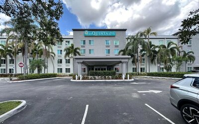 Exterior view of the hotel showcasing the main entrance, palm-lined surroundings, and convenient on-site parking at La Quinta Inn & Suites By Wyndham Sawgrass Mills.
