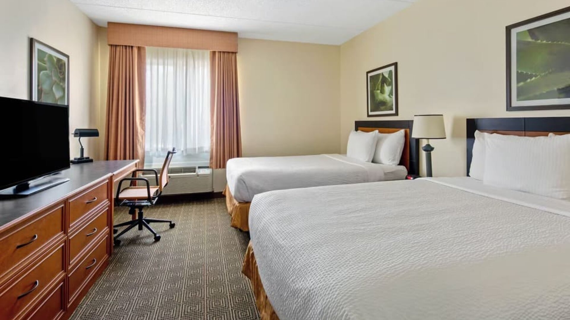 Guest room with two comfortable beds, a work desk, flat-screen TV, and modern amenities, offering a practical and relaxing stay for families, groups, or business travelers at La Quinta Inn & Suites By Wyndham Sawgrass Mills.