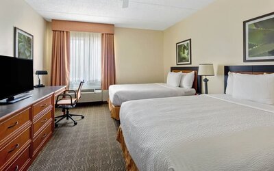 Guest room with two comfortable beds, a work desk, flat-screen TV, and modern amenities, offering a practical and relaxing stay for families, groups, or business travelers at La Quinta Inn & Suites By Wyndham Sawgrass Mills.