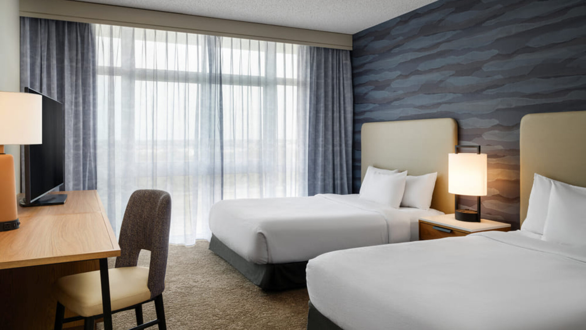 Guest room with two comfortable beds, modern furnishings, and floor-to-ceiling windows providing abundant natural light at Embassy Suites By Hilton Charleston Airport Convention Center.