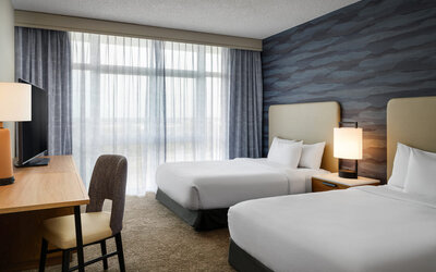 Guest room with two comfortable beds, modern furnishings, and floor-to-ceiling windows providing abundant natural light at Embassy Suites By Hilton Charleston Airport Convention Center.