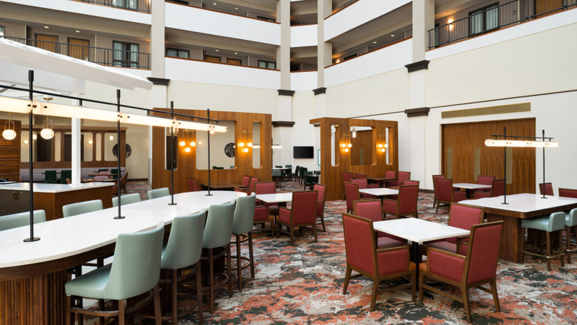 Atrium lounge area featuring communal tables, modern décor, and comfortable seating for socializing or informal meetings at Embassy Suites By Hilton Charleston Airport Convention Center.