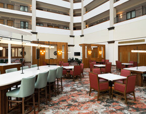 Atrium lounge area featuring communal tables, modern décor, and comfortable seating for socializing or informal meetings at Embassy Suites By Hilton Charleston Airport Convention Center.