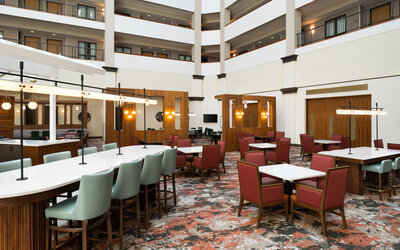 Atrium lounge area featuring communal tables, modern décor, and comfortable seating for socializing or informal meetings at Embassy Suites By Hilton Charleston Airport Convention Center.