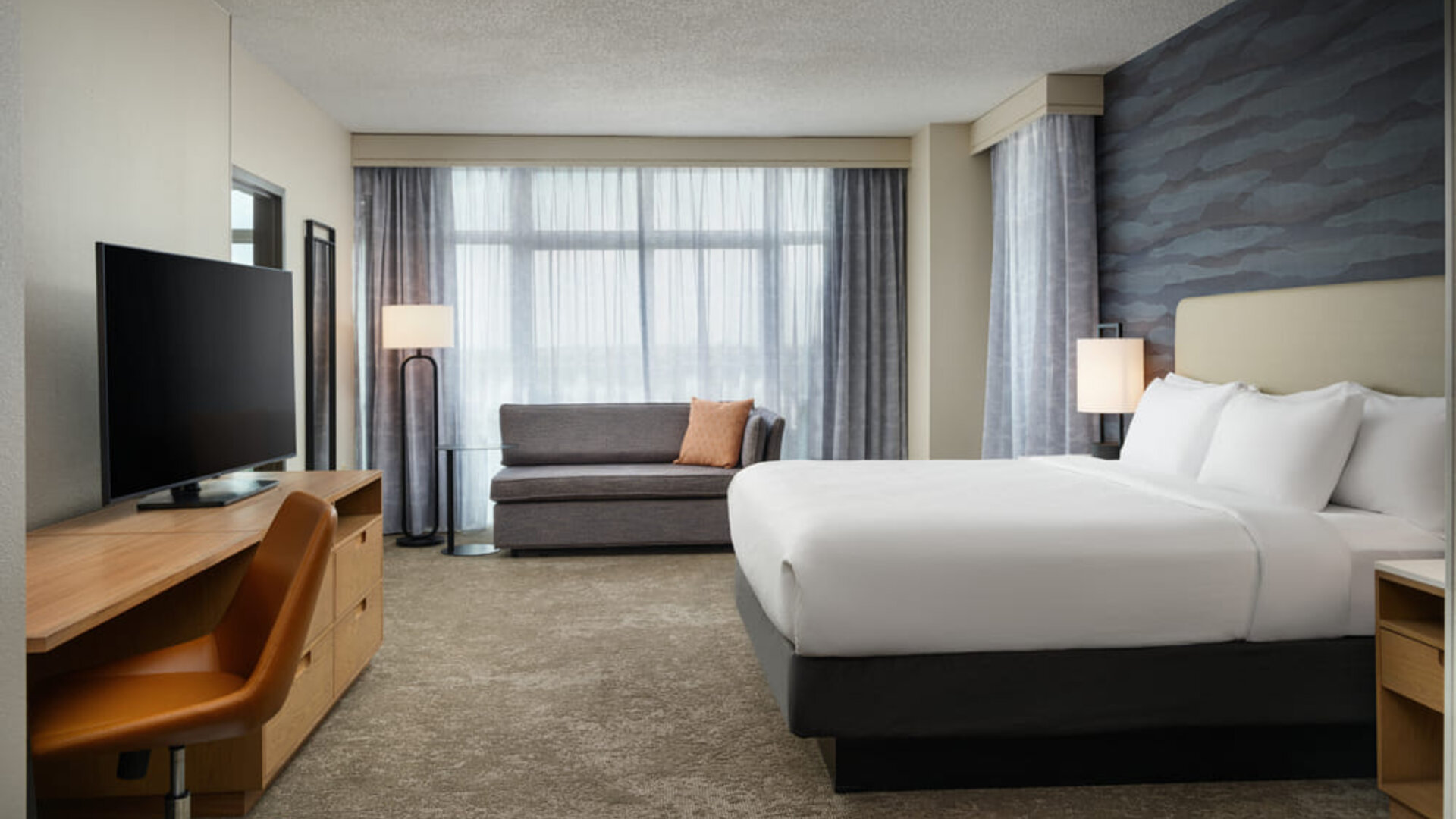King guest room featuring plush bedding, modern furnishings, and floor-to-ceiling windows for a comfortable stay at Embassy Suites By Hilton Charleston Airport Convention Center.