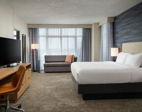King guest room featuring plush bedding, modern furnishings, and floor-to-ceiling windows for a comfortable stay at Embassy Suites By Hilton Charleston Airport Convention Center.
