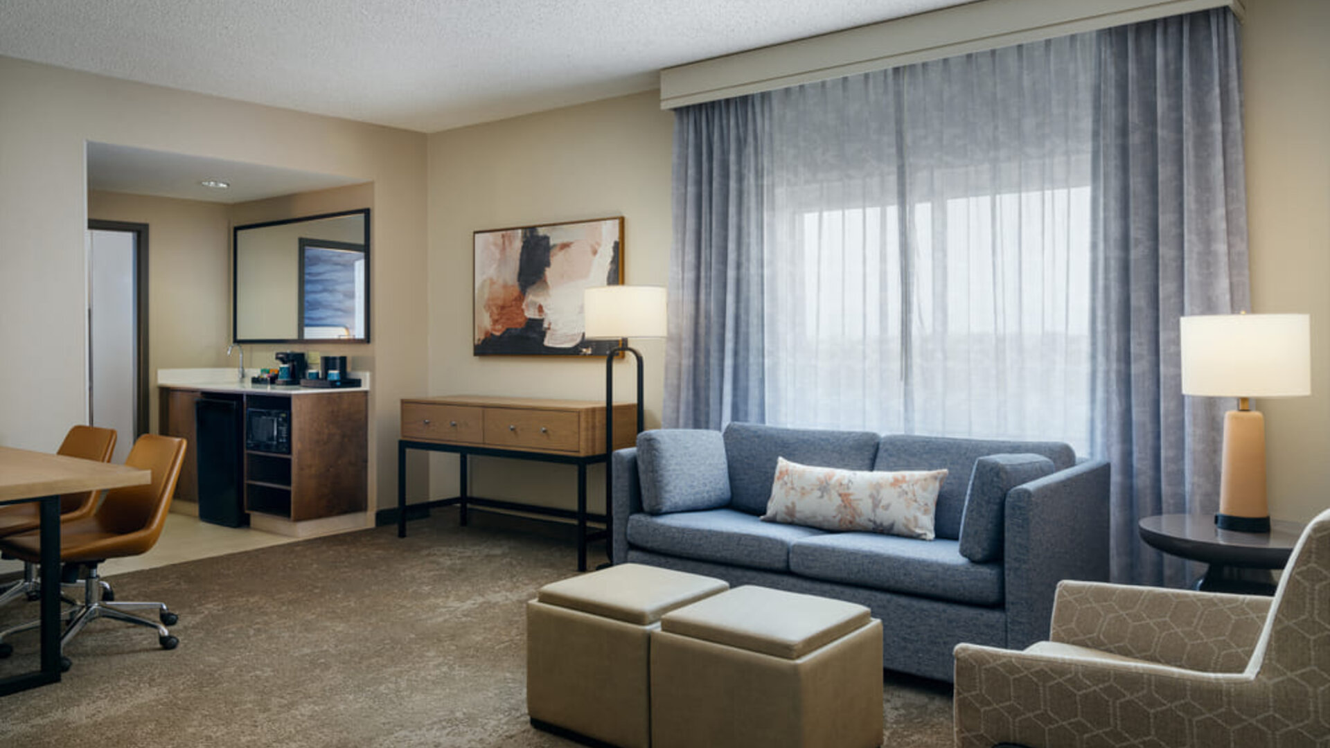 Spacious suite living area with comfortable sofa seating, work space, mini refreshment station, and large windows providing natural light at Embassy Suites By Hilton Charleston Airport Convention Center.