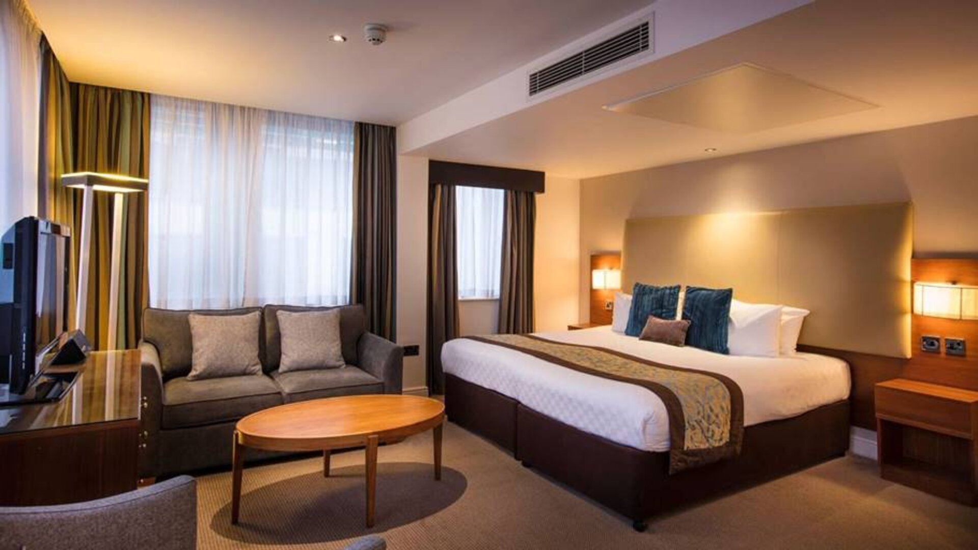 Wide view of the Thistle Trafalgar Square executive king room, featuring large bed, sofa, and TV.