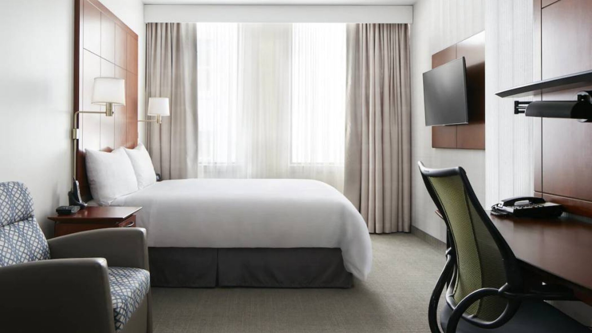 Guest room in the Club Quarters Hotel Central Loop, furnished with large double bed and desk/chair for working.