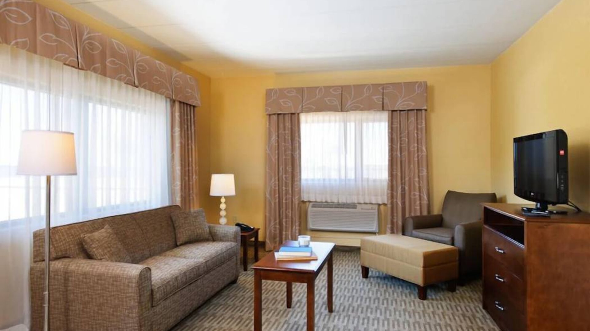 Guest room lounge in Holiday Inn Express Philadelphia Airport, with sofa, chair, TV, and foot stool.