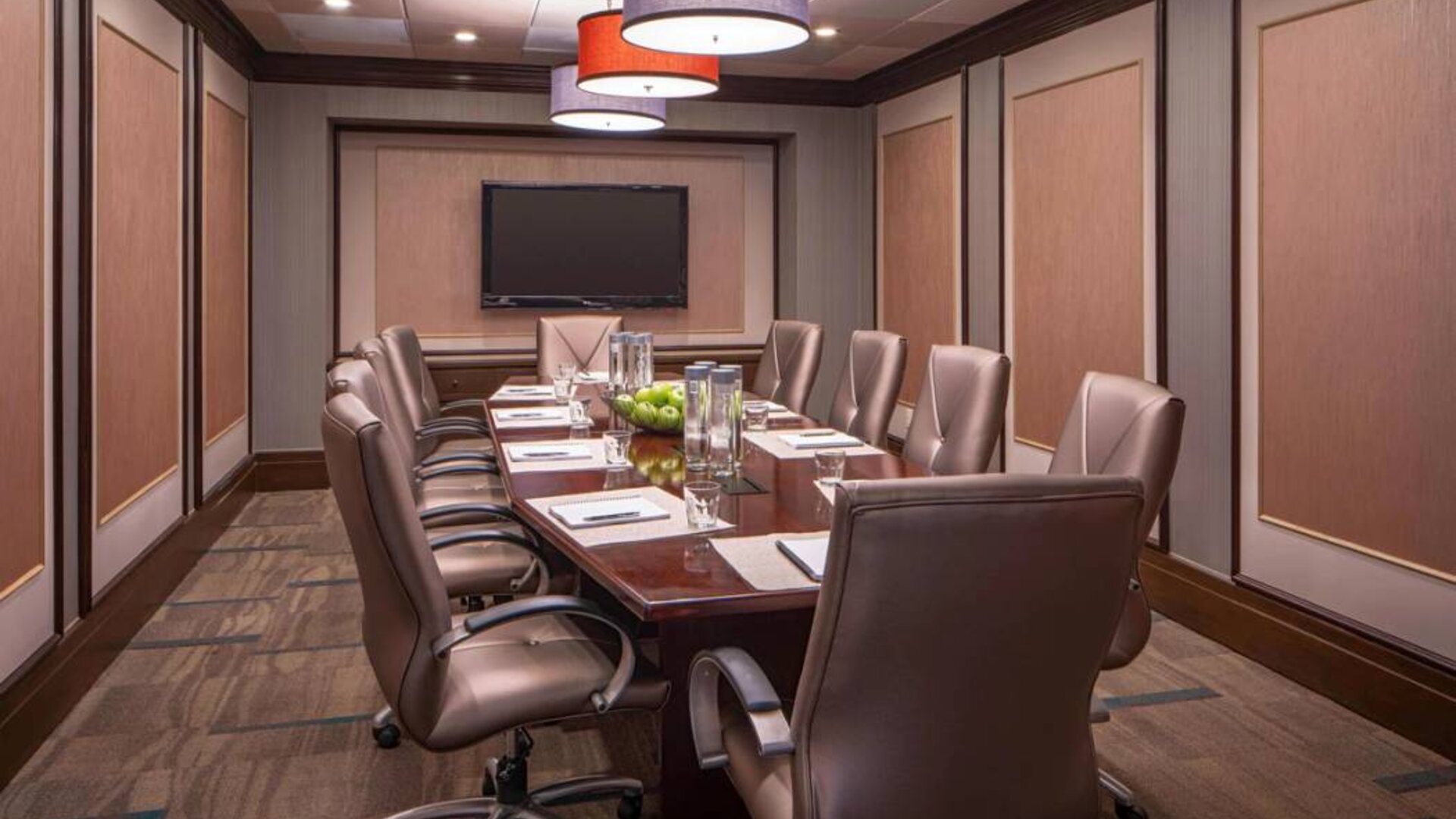 Hotel meeting room, featuring long wooden table and surrounding leather chairs.