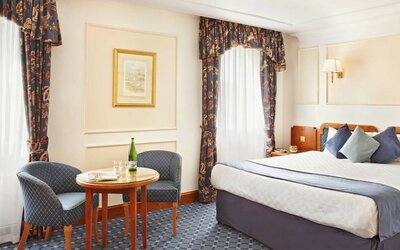 An executive double standard room at the Thistle London Heathrow Terminal 5, with large bed, windows, and coffee table and chairs.