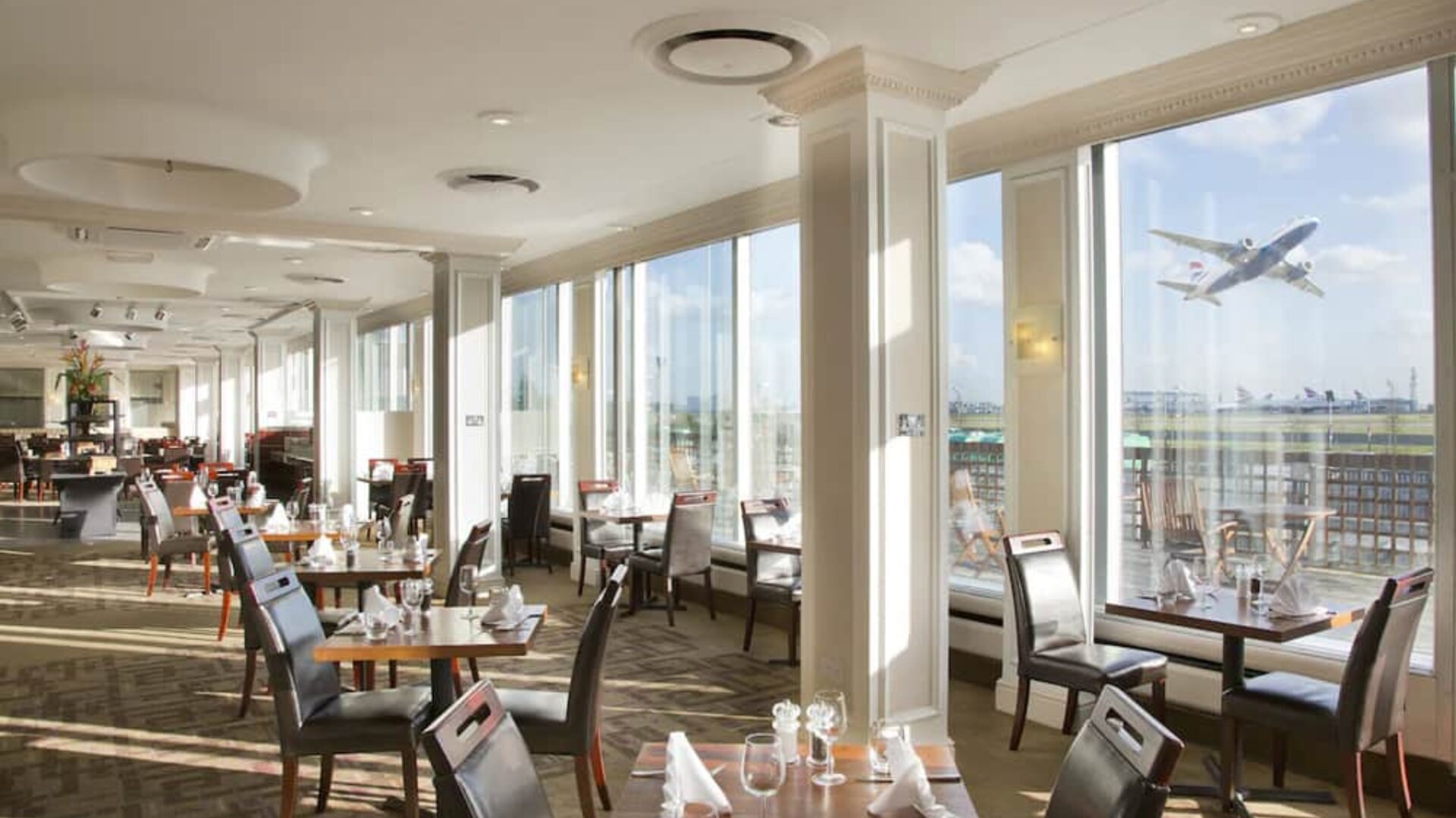 Sunlight room with floor to ceiling windows spanning the entire length of the wall to see planes takeoff and land at London Heathrow Airport.