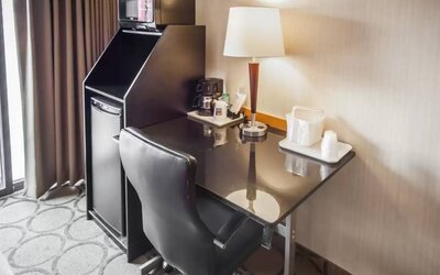 Closer shot of an in-room workspace, including chair, desk, lamp, and nearby window.