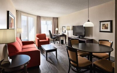 Guest room lounge in Les Suites Hotel Ottawa, with workspace desk and chair, plus sofa, chairs, and tables.